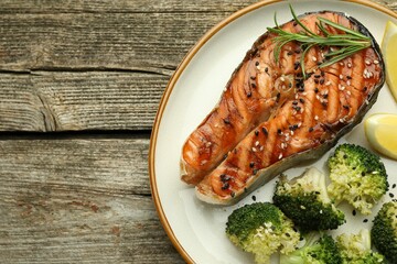 Tasty grilled salmon steak, broccoli, lemon and rosemary on wooden table, top view. Space for text