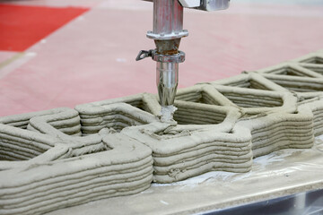 A large 3D printer steadily layers concrete, forming the walls of a house on a construction site.