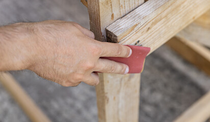 Young adult man hand using dark sandpaper sponge and sanding light wooden surface. Close Up. Preparing material for repair work of home. Empty place for text.