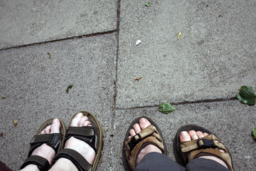 Two pairs of feet in walking sandals and pavement - Durham - England - UK