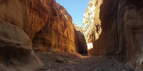 Obraz premium A narrow canyon with towering rock walls and a rocky floor under a clear blue sky.