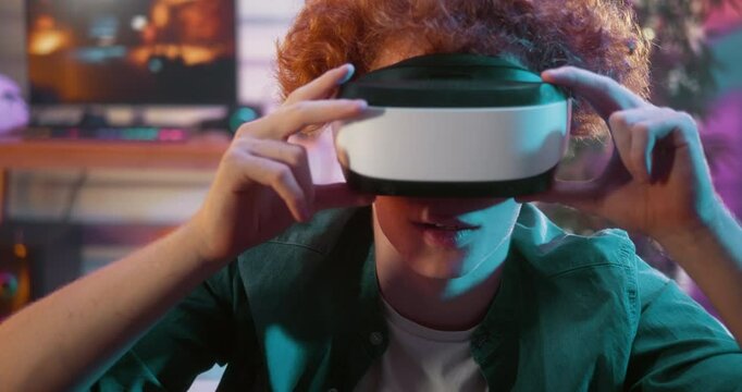 Teeh boy puts on virtual reality goggles, feels  excited while enjoying playing games at home in neon light room