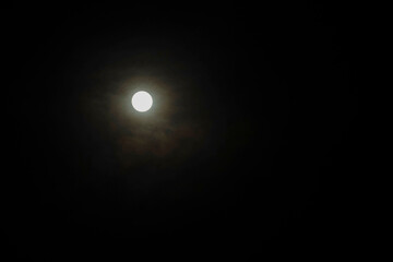 Full moon glowing in a dark night sky with a subtle cloud haze surrounding it. Aruba.