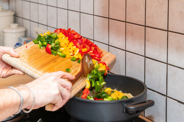 Wooden cutting board with freshly cut green, yellow, red paprika, peppers on the kitchen countertop. Close-up view. Healthy food cooking, home made healthy dinner. Fresh vegetables