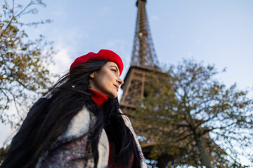 A young woman in a red beret gazes thoughtfully at the Eiffel Tower on a breezy day in Paris. Woman...