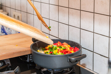 A cooking pot on gas fire. Person putting fresh cut paprikas from a wooden cutting board into a cooking pot on gas stove. The gas fire is on. Healthy food cooking, home made healthy dinner. Fresh vege