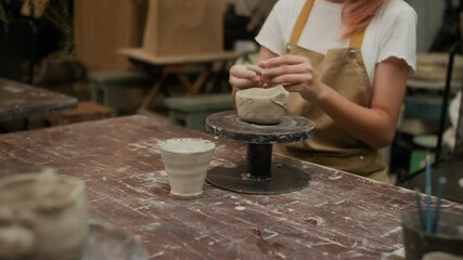 Rack focus of unrecognizable schoolkids in aprons sculpting cups with animal faces from clay during pottery class