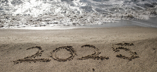 tropical New Year 2025 written in sand on the beach