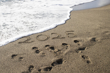 tropical New Year 2025 written in sand on the beach