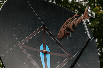 A creatively painted satellite dish features a fish skeleton decoration and geometric patterns in a...