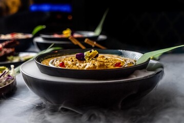 Roasted butternut chicken squash soup decorated with maroon and yellow flowers, and pomegranate served on a dinner table with more mouthwatering foods