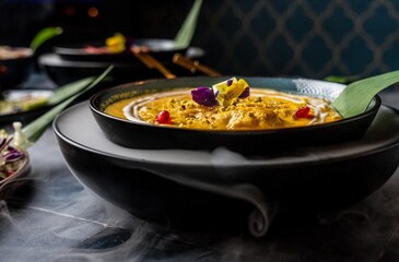 Roasted butternut chicken squash soup decorated with maroon and yellow flowers, and pomegranate served on a dinner table with more mouthwatering foods
