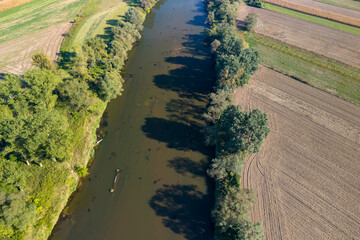 Aerial view of a calm river surrounded by lush greenery and agricultural fields, showcasing the...