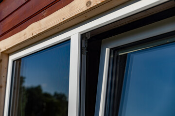 Close-up of a white window frame with a metal hinge and a chain mechanism. The window is open, revealing a view of blue sky. The image captures the details of the window's construction. - Powered by Adobe