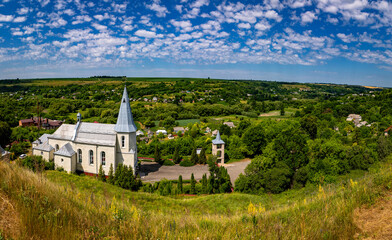 Fototapeta premium Catholic church in the Ukrainian village of Zinkiv. Rural landscape with a beautiful church on a summer day.