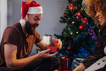Bearded man opening christmas gift with girlfriend near christmas tree