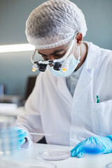 Vertical shot of African American male microbiology scientist wearing magnifying glasses working...
