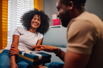 Diverse couple having a festive couch conversation with wrapped gift in hand