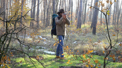 Naklejka premium A man in a hat with a backpack takes pictures in the forest. Travel concept