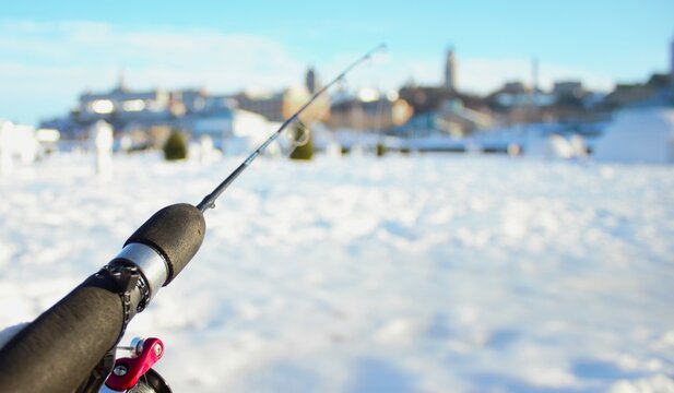 Fishing Rod on a Frozen Lake with Snow-Covered Buildings in the Background