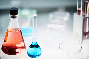 Close up on two glass beakers filled with red and blue chemical solutions resting on light table in laboratory of scientific research service, copy space