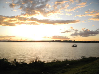 pequeno barco navegando em lago em um  final de tarde de um dia com nuvens rosadas no céu.