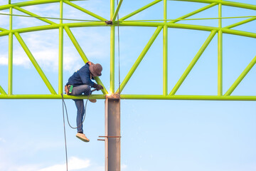 Obraz premium Welder is welding metal of industrial warehouse building structure against blue sky in construction site area