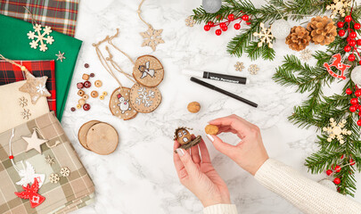 Woman makes Christmas craft toys from natural materials: nuts, wood, cardboard. Handmade christmas gift. Top view. Christmas eve preparation. Female hands holding a DIY Christmas toy. Natural rustic