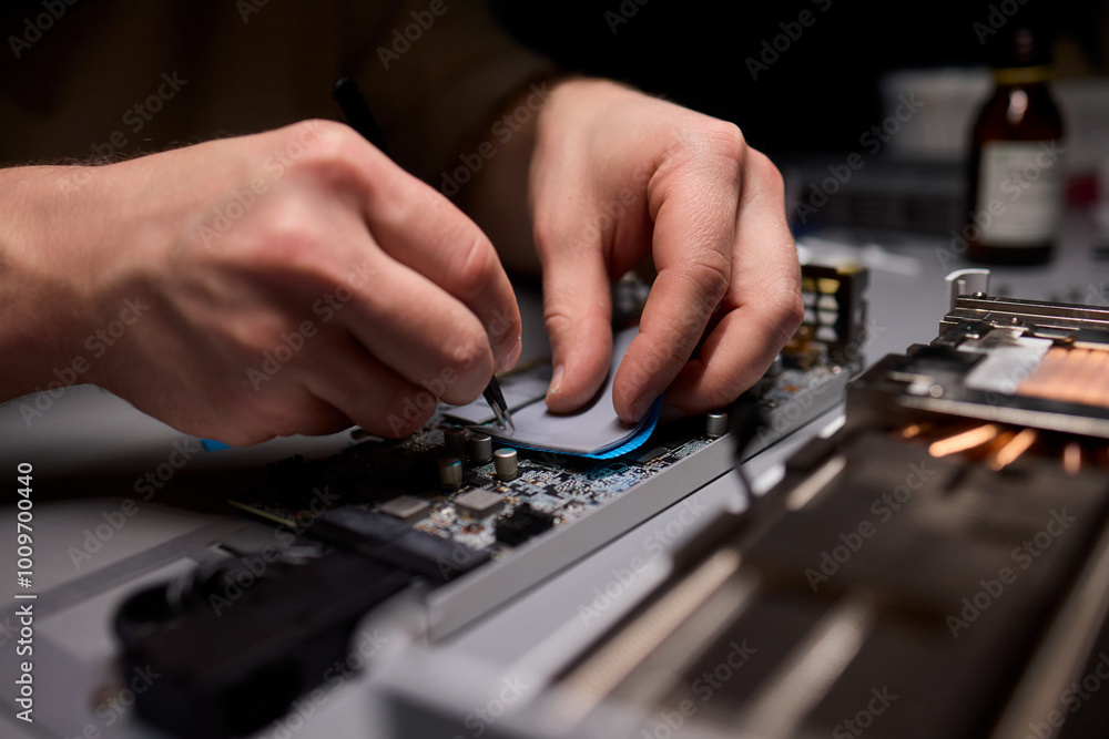 Poster hand repairing a graphics card through the application of thermal paste for better performance