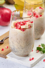 A glass of chia seeds and yogurt, with banana pieces and pomegranate seeds added to the dessert