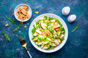 Foodie food salad with crispy apple, celery, lettuce, griled chicken slices, arugula and walnuts on blue background, top view