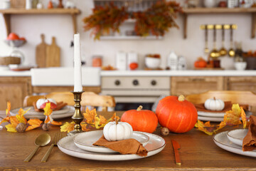 Dinning table setting for fall dinner, with pumpkins, leaves, and candle on kitchen background