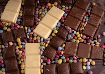 photo an assortment of chocolate bars and colorful candy-coated chocolates. There are various kinds of chocolate bars, including white chocolate and dark chocolate, scattered among the multicolored 