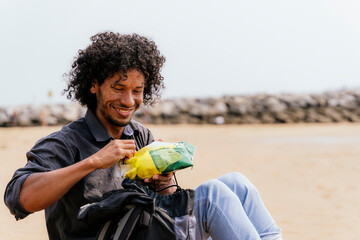 Young man smiling with snack on sandy beach