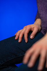 A female sitting on a chair in purple knitted sweater hands are on her laps. Woman's hands are down. Feeling powerless in some circumstances.