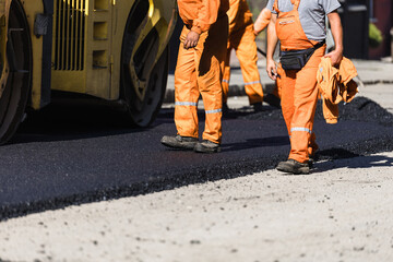 Construction workers in orange uniforms paving a road with asphalt during a sunny day in a city