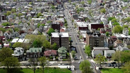 Aerial footage capturing the urban landscape of Northern New Jersey, featuring a mix of residential neighborhoods, industrial areas, and the iconic New York City skyline in the distance. 
