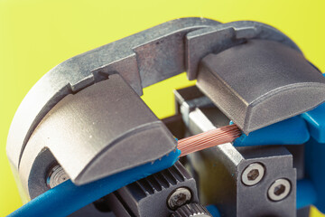 Close-up of a wire stripper tool cutting a blue wire with exposed copper. Macro shot of electrical equipment.