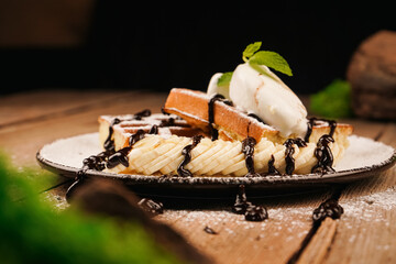 Belgian waffles with banana, ice cream and chocolate on top. Served with ice cream. Sweet dessert waffles. Delicious dessert for tea time. Mint on top of dessert. Cooking process.