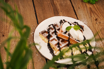 Cooking process. Served with ice cream. Belgian waffles with banana, ice cream and chocolate on top. Sweet dessert waffles. Delicious dessert for tea time. Mint on top of dessert.