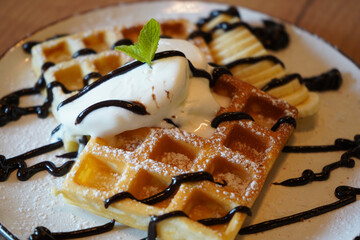 Belgian waffles with banana, ice cream and chocolate on top. Sweet dessert waffles. Waffle on wooden table. Cooking process. Top view. Served with ice cream. Delicious dessert for tea time.