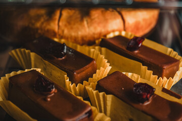 A display case with a variety of cakes and cupcakes. Chocolate deserts with cherry on the top. The...