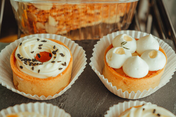 The tarts with mango and tarts with dork cheese are arranged in a row on black plate. Display case...