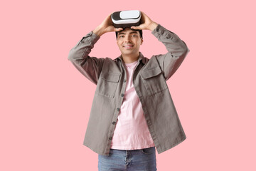 Happy young man with VR glasses on pink background