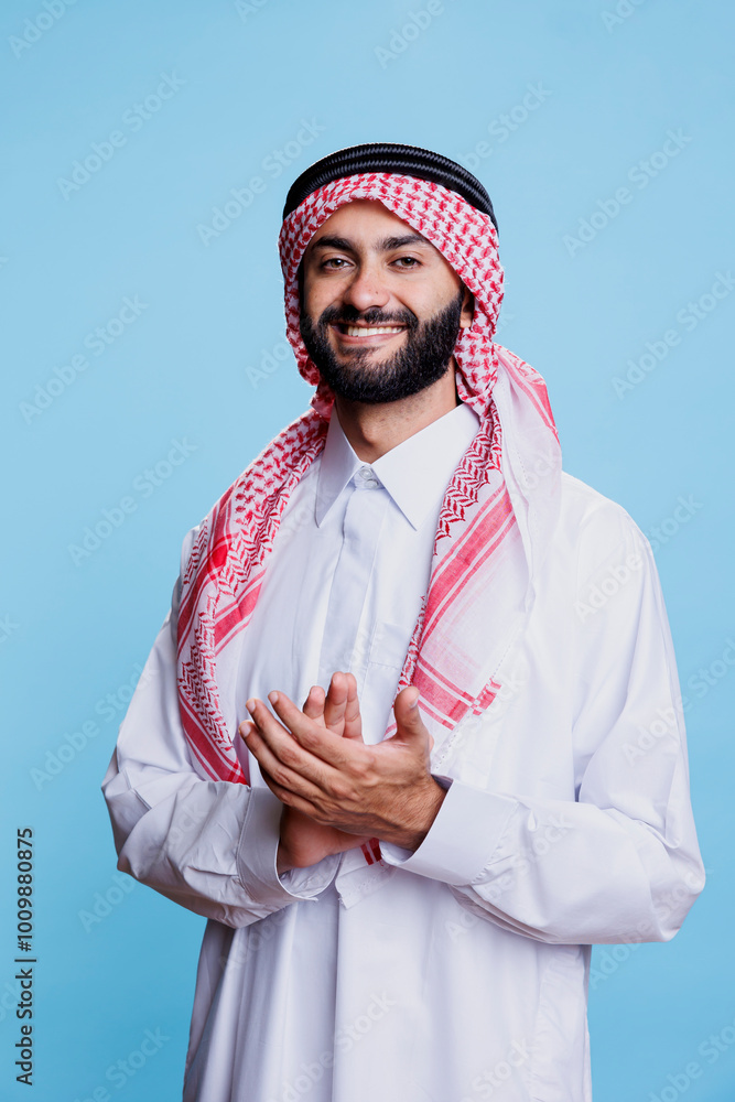 Poster muslim man wearing traditional clothes displaying support gesture by applauding with hands in studio