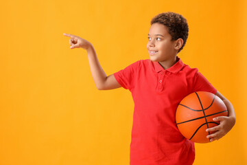 Little African-American boy with ball pointing at something on yellow background