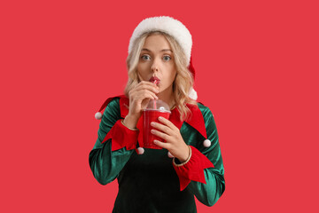 Young woman dressed as elf drinking cola on red background
