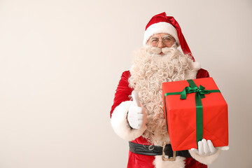 Santa Claus with Christmas gift showing thumb-up on white background