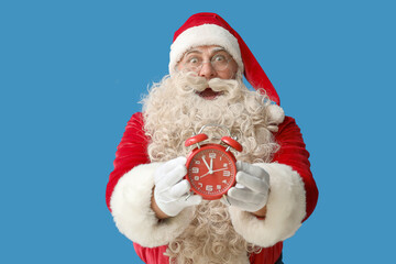 Shocked Santa Claus with alarm clock on blue background