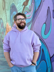 Millennial man in a pastel hoodie standing in front of a vibrant, abstract mural. Soft fabric and bold graffiti creates a striking contrast of modern urban style. Street urban style fashion